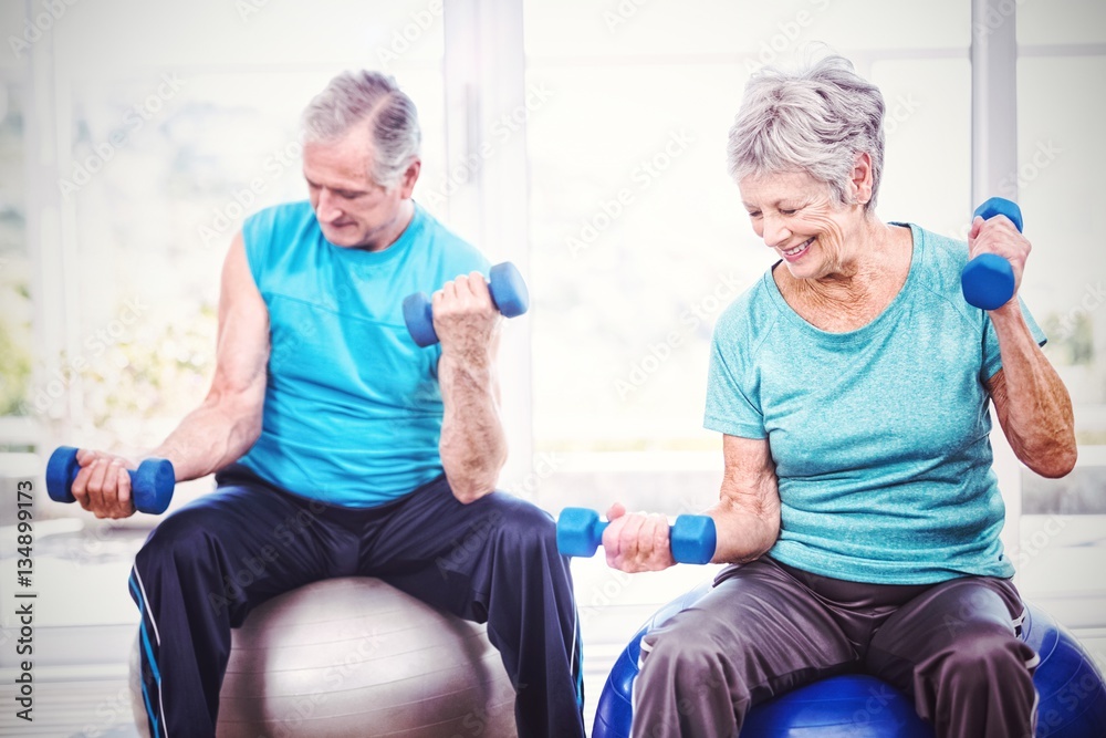 Smiling senior couple holding dumbbells while exercising