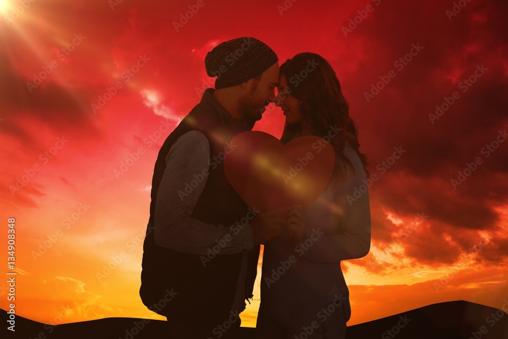 Composite image of happy young couple holding heart shape paper