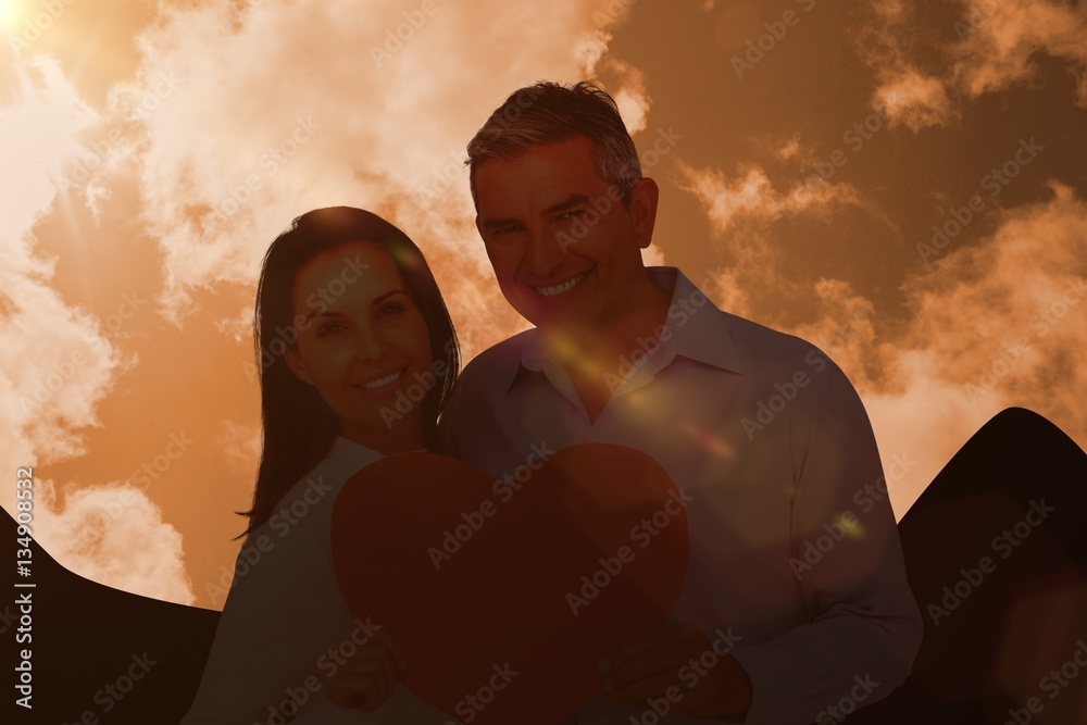 Composite image of happy couple holding big heart shape paper