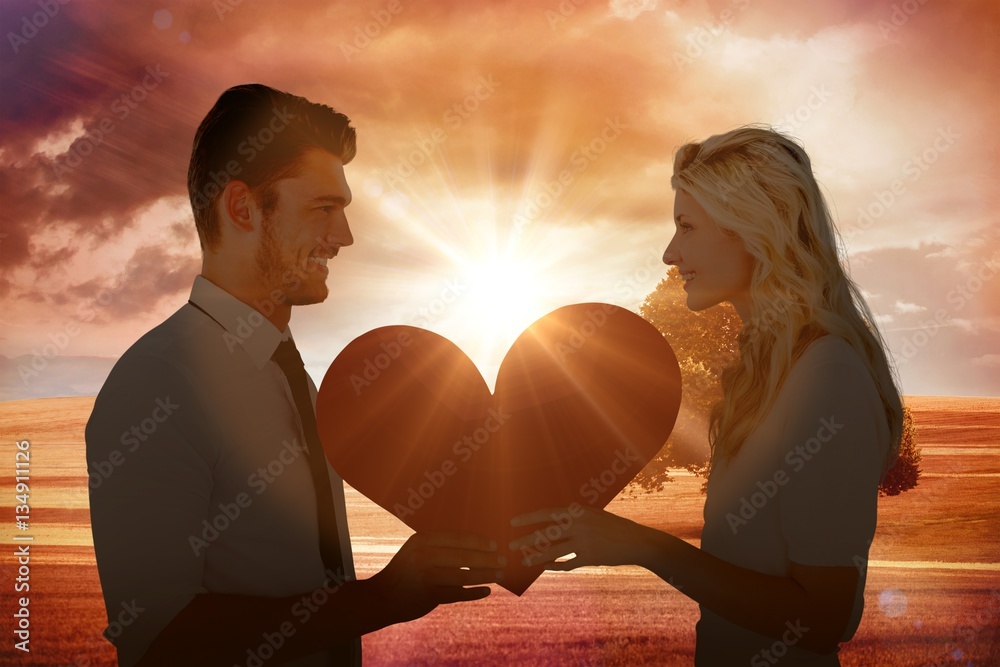 Composite image of attractive young couple holding red heart