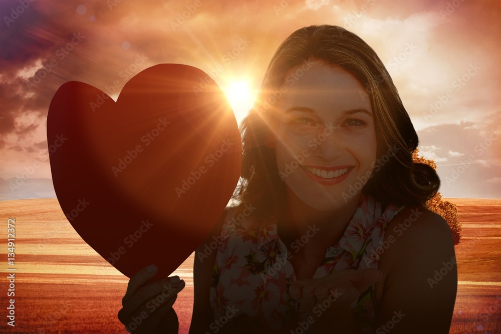 Composite image of woman holding heart card and blowing kiss