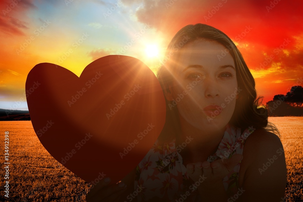 Composite image of woman holding heart card and blowing kiss