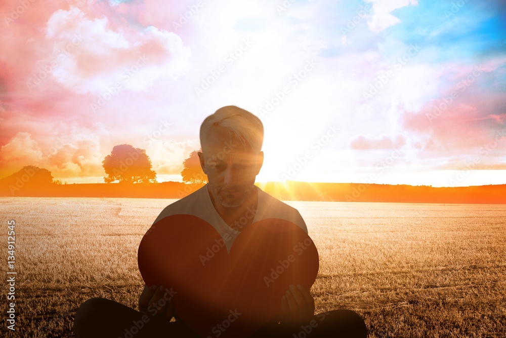 Composite image of upset man sitting holding heart shape