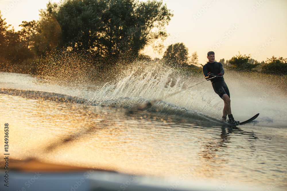 Man wakeboarding on lake behind motorboat