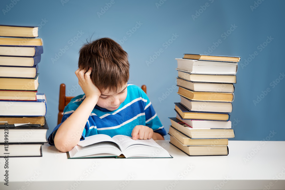 seven years old child reading a book at home. Boy studing at table on blue background