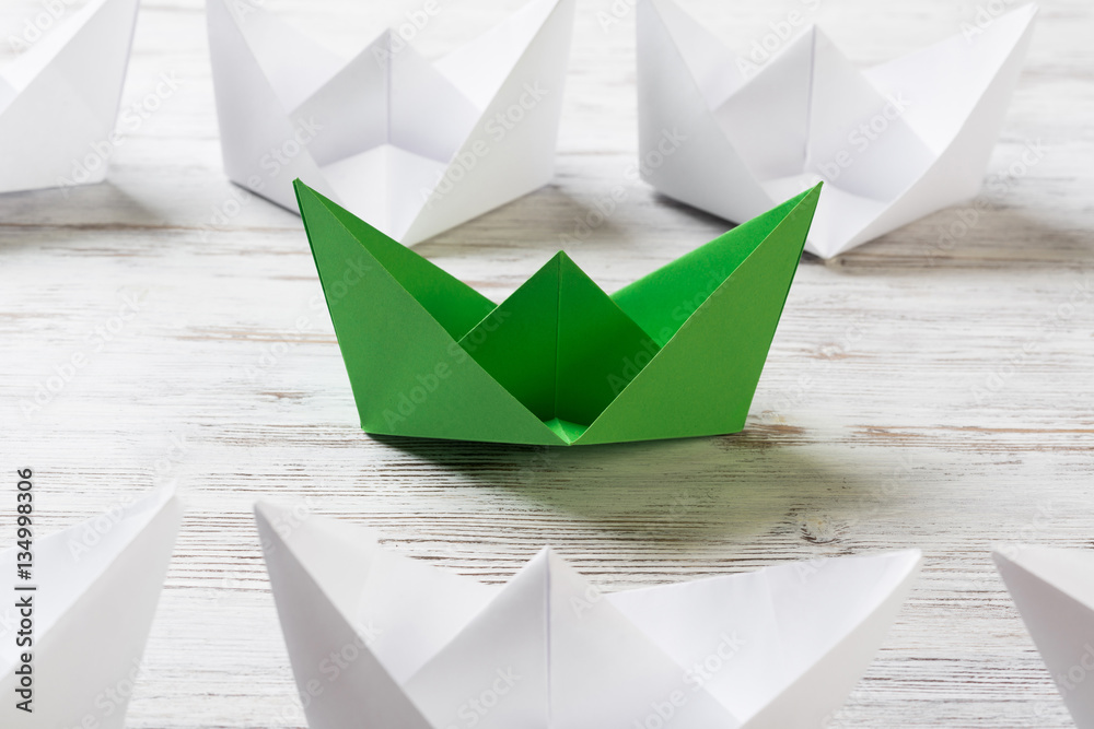 Business leadership concept with white and color paper boats on wooden table