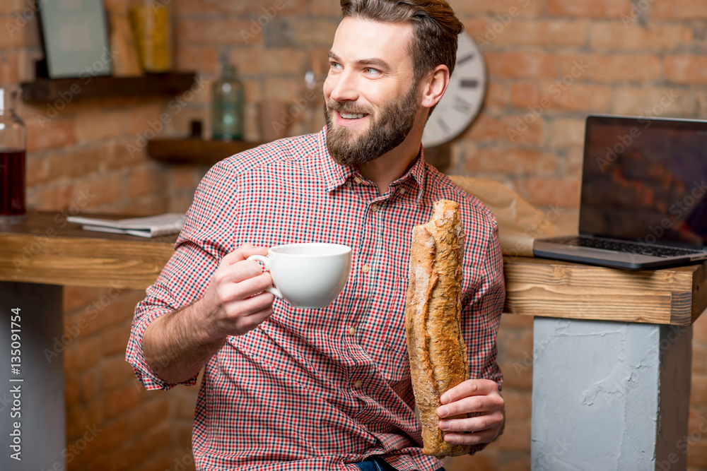 Handsome man having breakfast with coffee and baguette at the kitchen