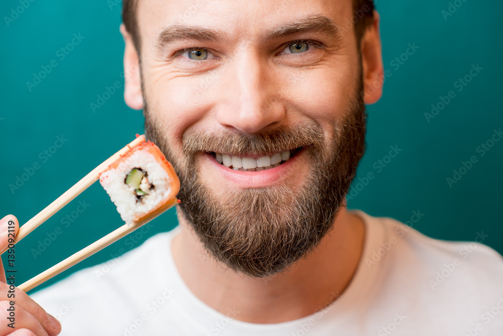 Close-up portrait of a man holding sushi with chopsticks on the green background