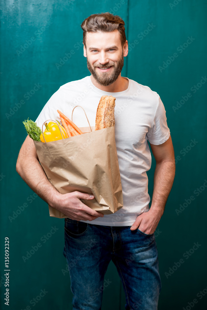 Handsome man holding a paper bag full of healthy food on the green background