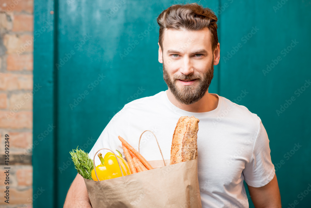 Handsome man holding a paper bag full of healthy food on the green background