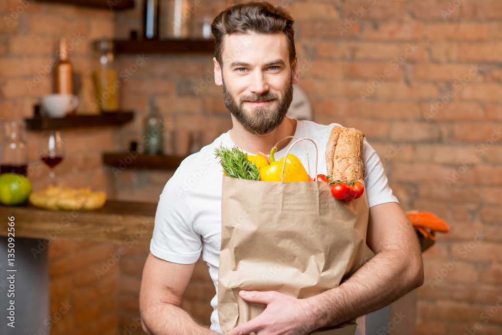 Handsome man holding a paper bag full of healthy food in the kitchen