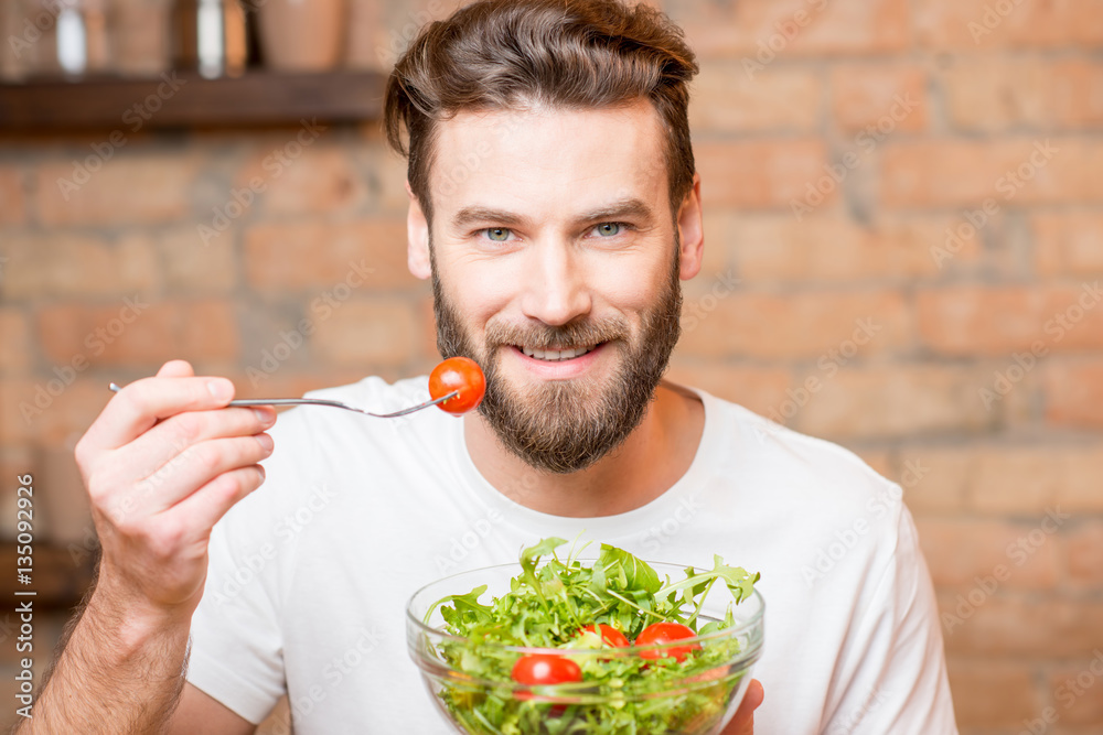 Close-up portrait of a man eating salad with tomatoes on the red brick wall background. Healthy and 