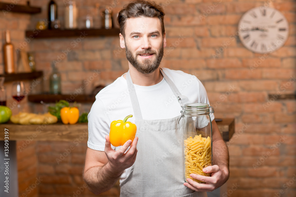 Portrait of a healthy man holding yellow pepper and jar with pasta on the kitchen