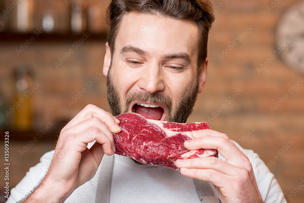 Handsome man biting raw meat on the kitchen