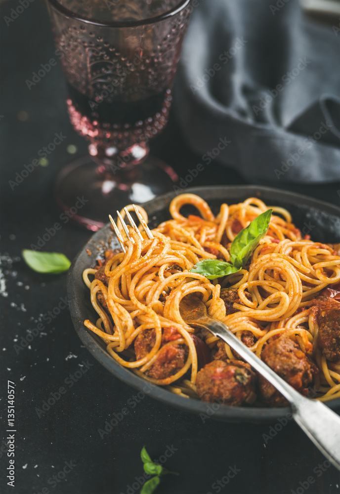 Italian pasta dinner. Spaghetti with meatballas, fresh basil leaves in dark plate and red wine in vi