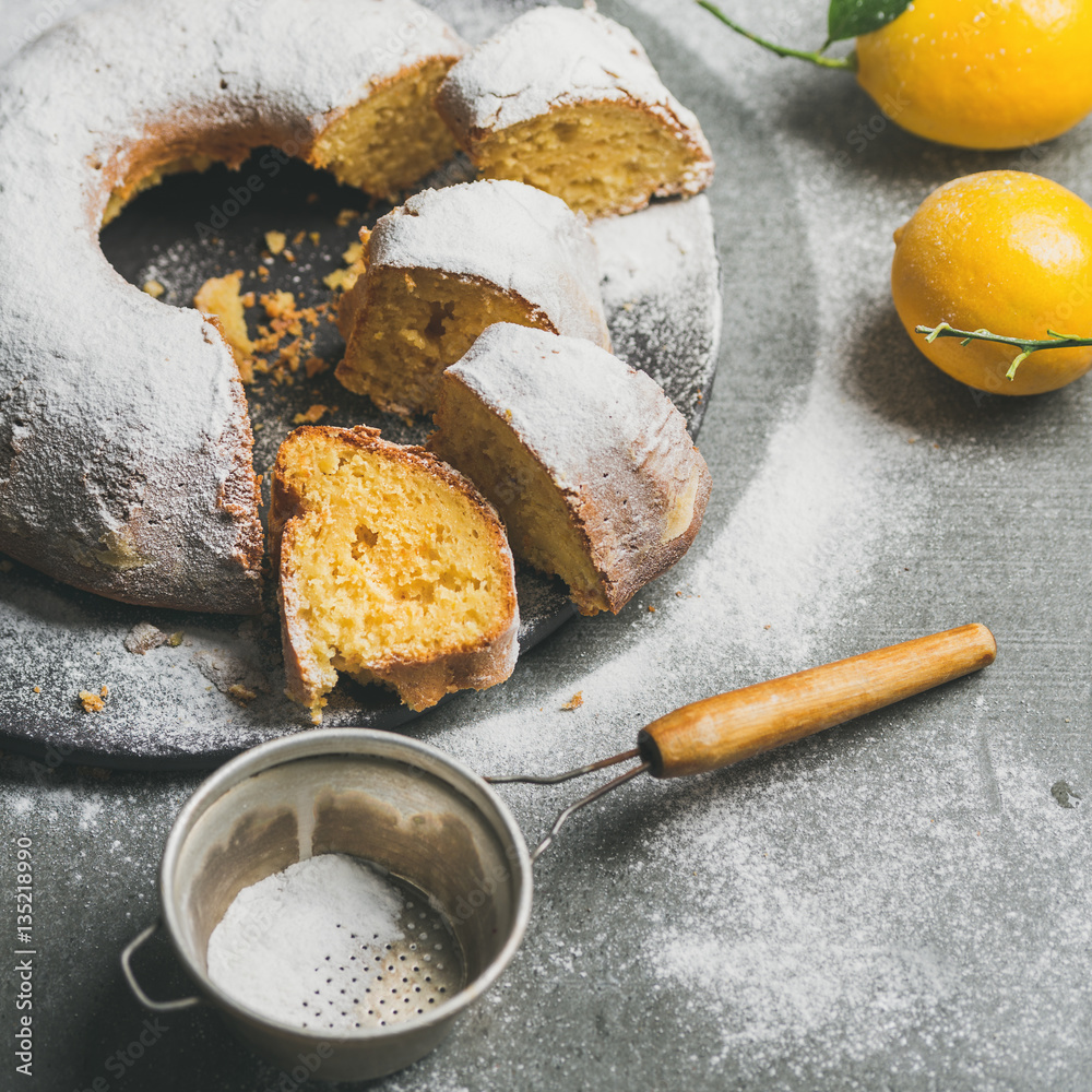 Homemade gluten-free lemon bundt cake with sugar powder over grey concrete background, selective foc