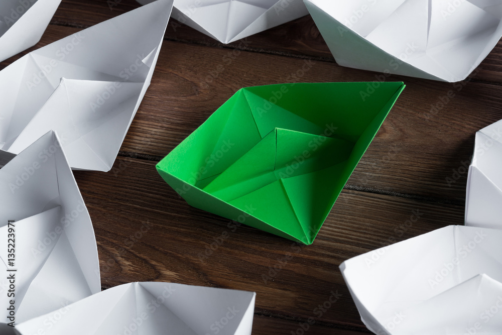 Business leadership concept with white and color paper boats on wooden table