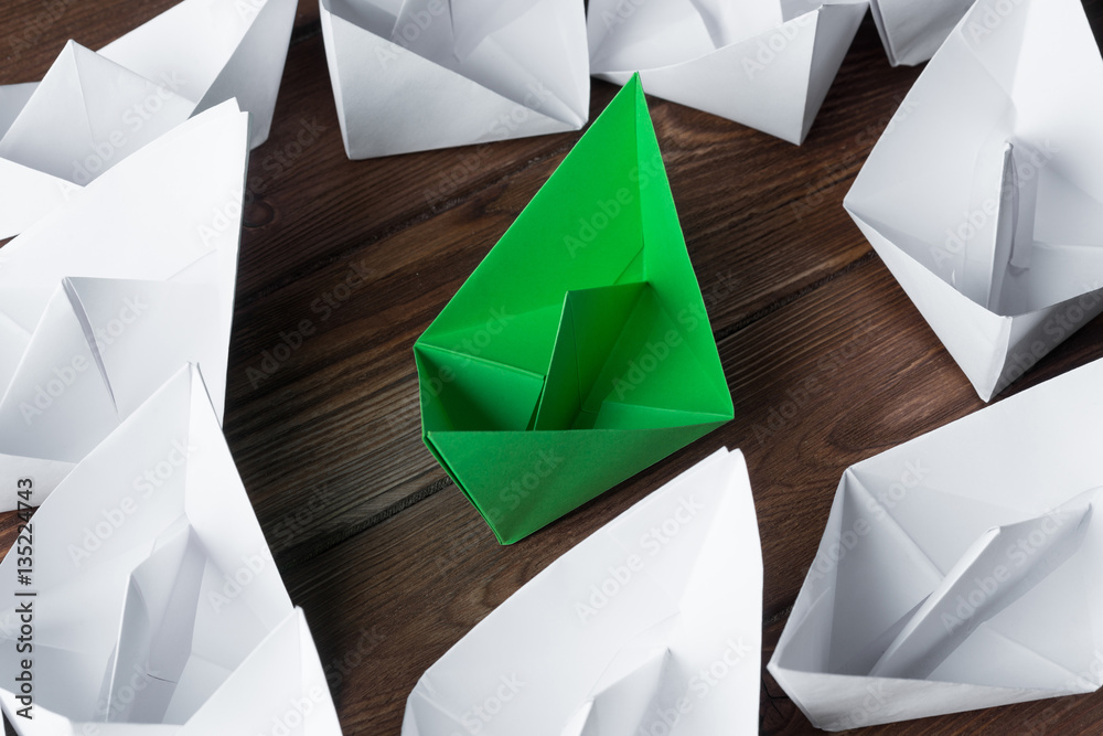 Business leadership concept with white and color paper boats on wooden table