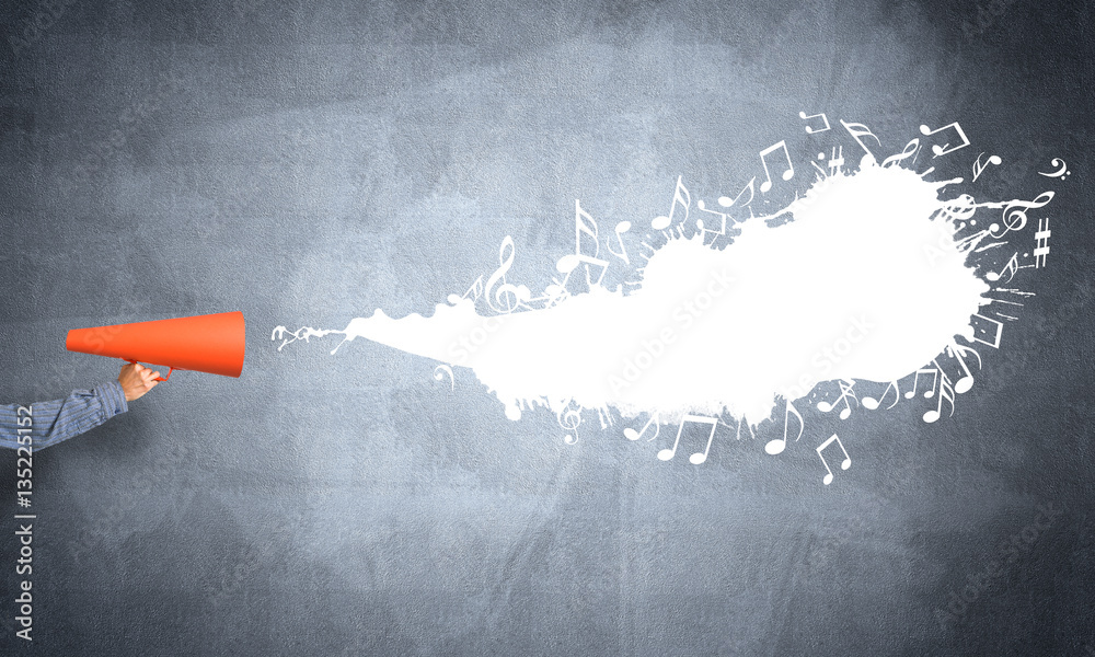 Hand of man holding orange paper trumpet against concrete background