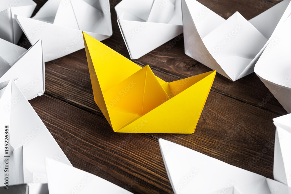 Business leadership concept with white and color paper boats on wooden table