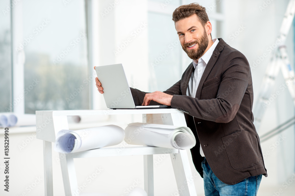 Architect or designer working with laptop on the ladder with paper drawings in the bright room for r