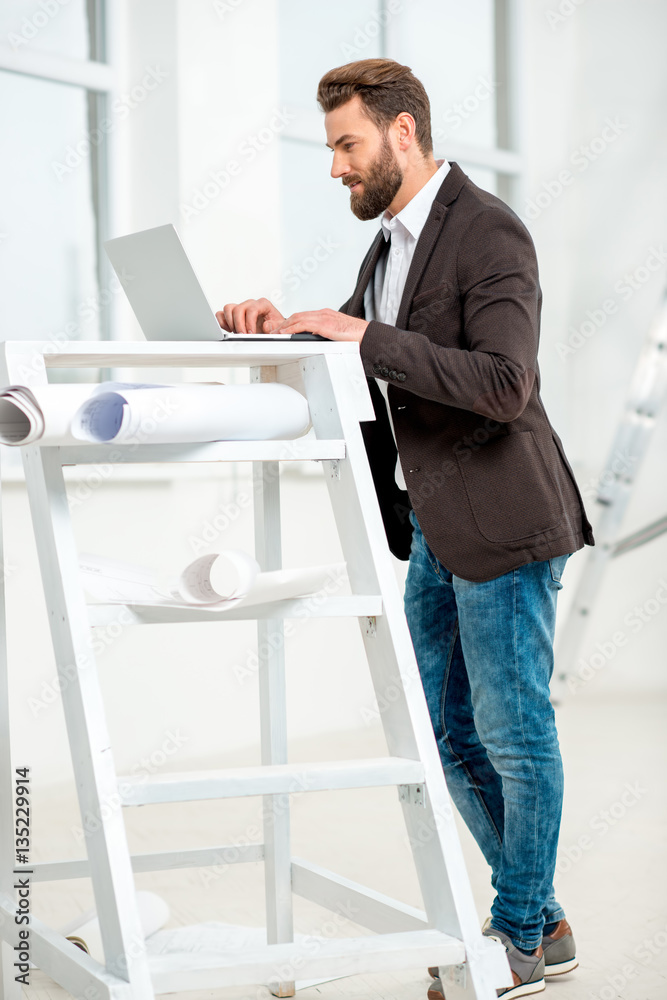 Architect or designer working with laptop on the ladder with paper drawings in the bright room for r