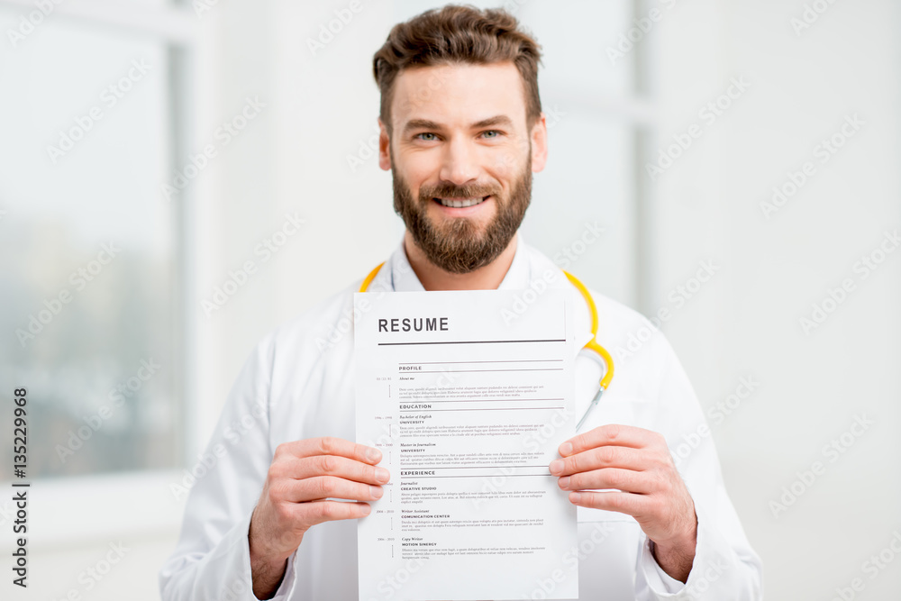 Doctor in uniform holding resume for job hiring in the white interior. Image focused on the paper an