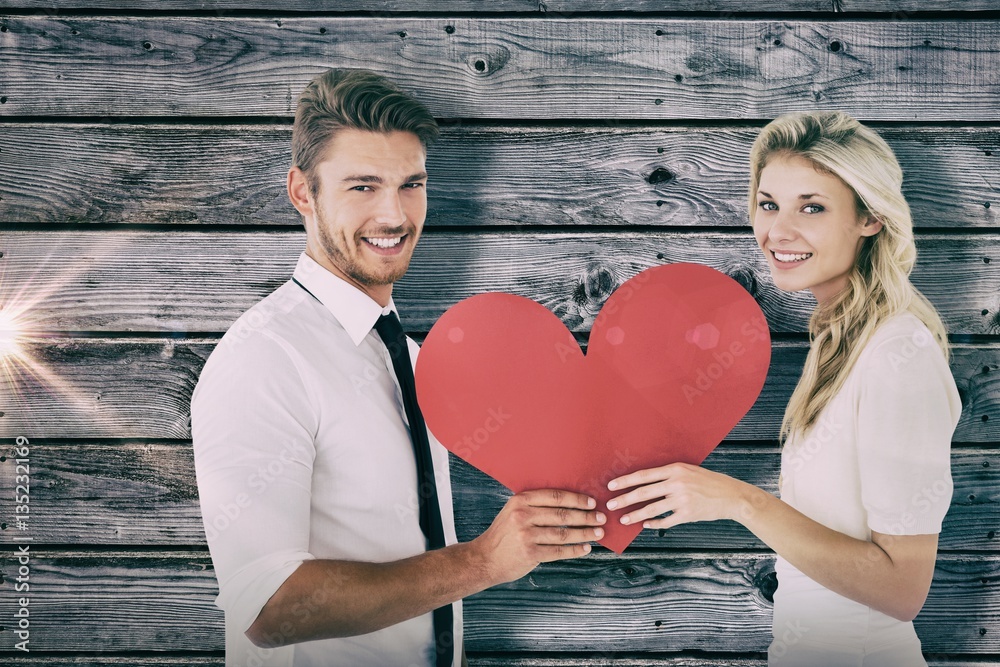 Composite image of attractive young couple holding red heart