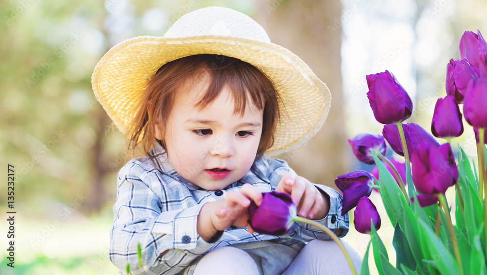 Toddler girl in a hat playing with tulips