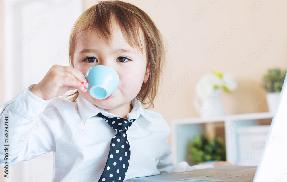 Toddler girl drinking from a mug in front of a laptop