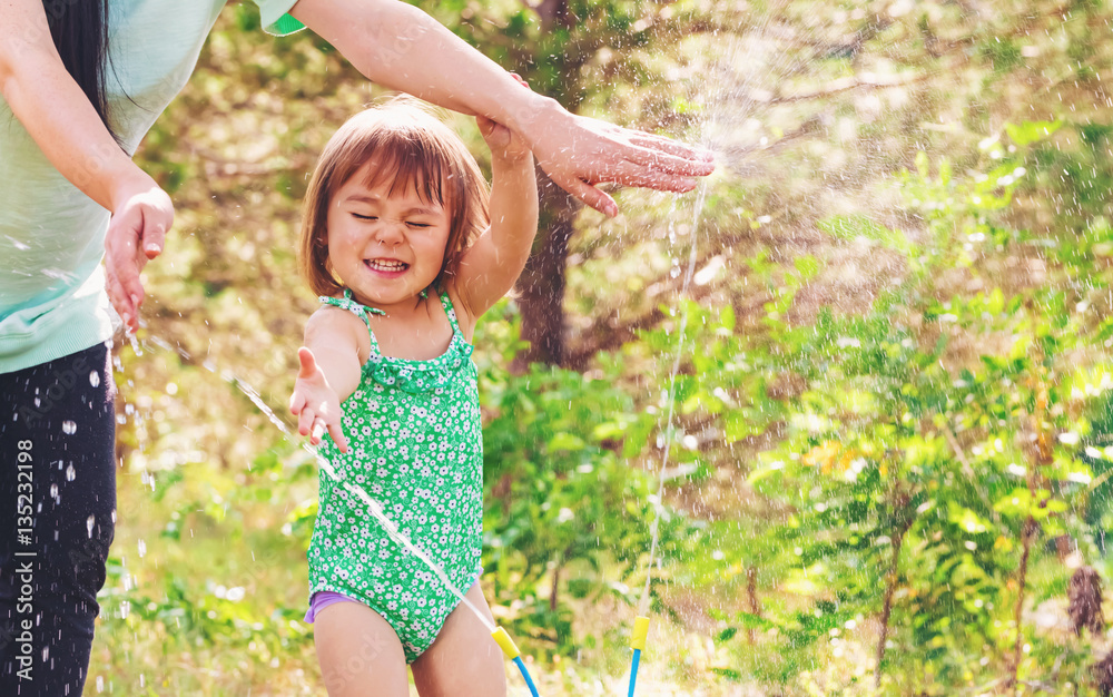 Toddler girl playing in a sprinkler with her mother