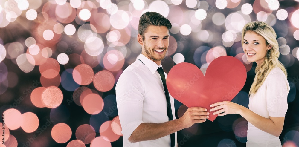 Composite image of attractive young couple holding red heart