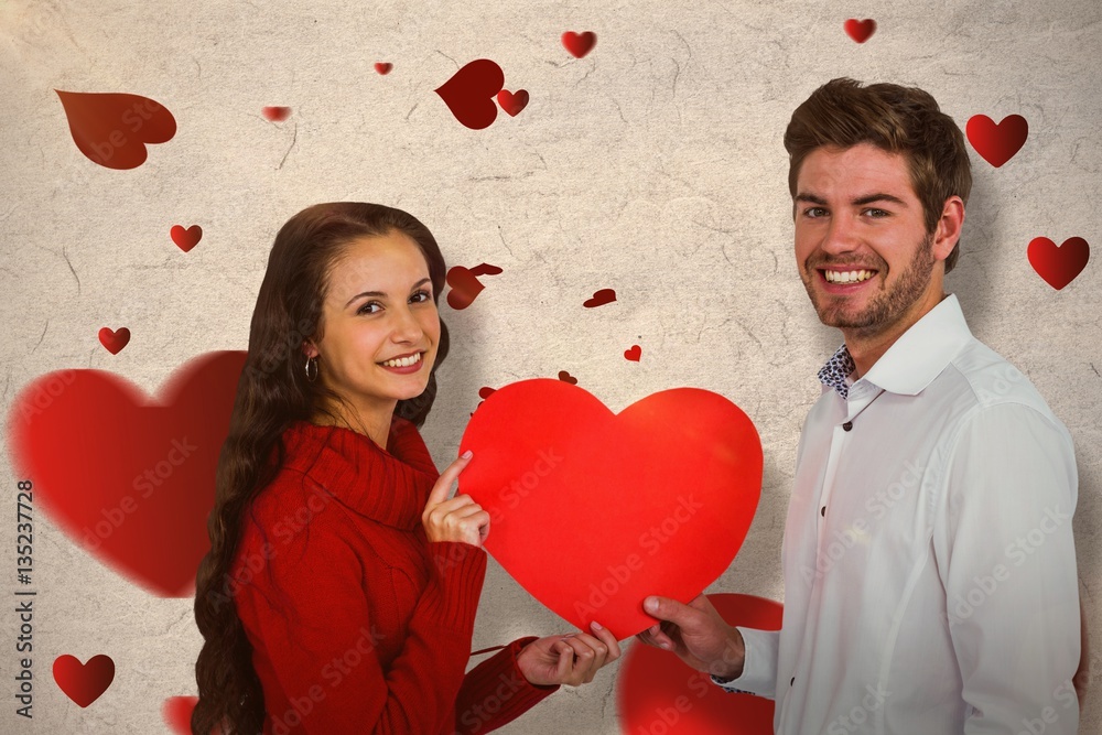 Composite image of smiling couple holding paper heart