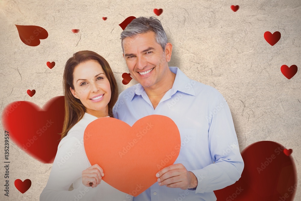 Composite image of happy couple holding big heart shape paper