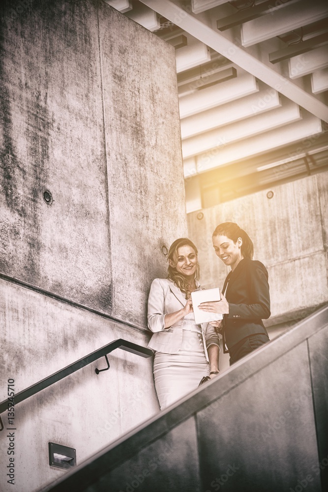 Businesswomen standing on staircase and using tablet 