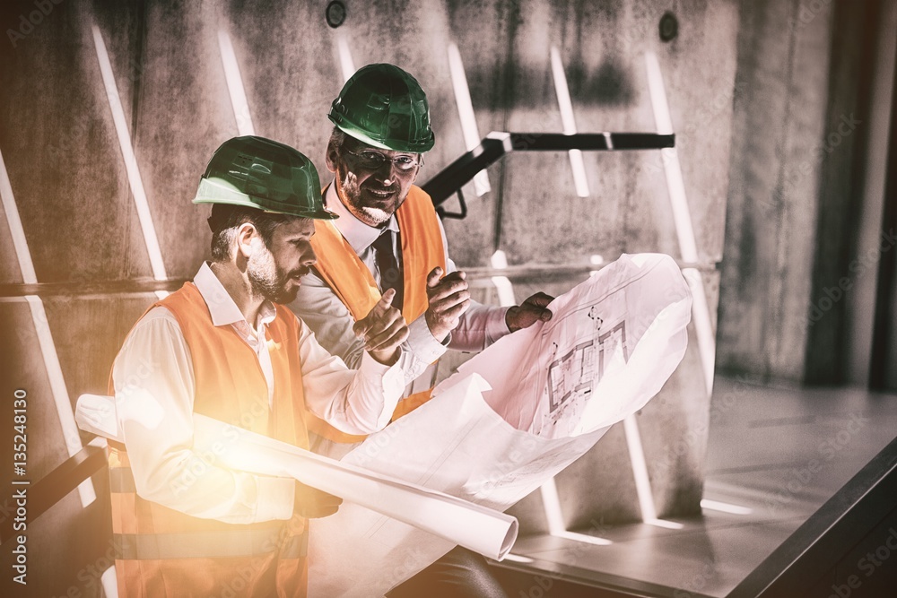 Architects standing on staircase discussing with blueprint