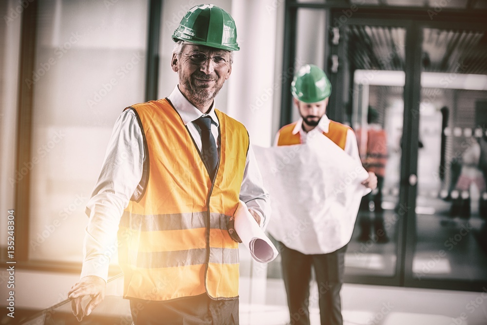 Architect in hard hat standing with blueprint in office corridor