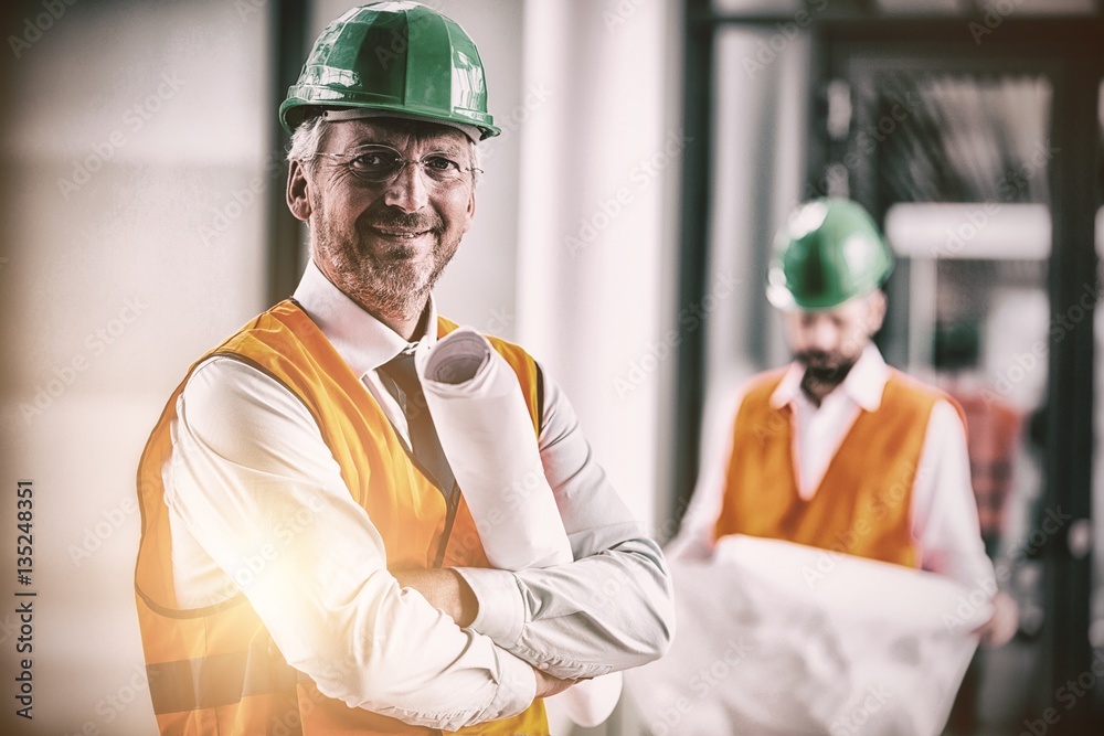 Architect in hard hat standing with blueprint in office corridor