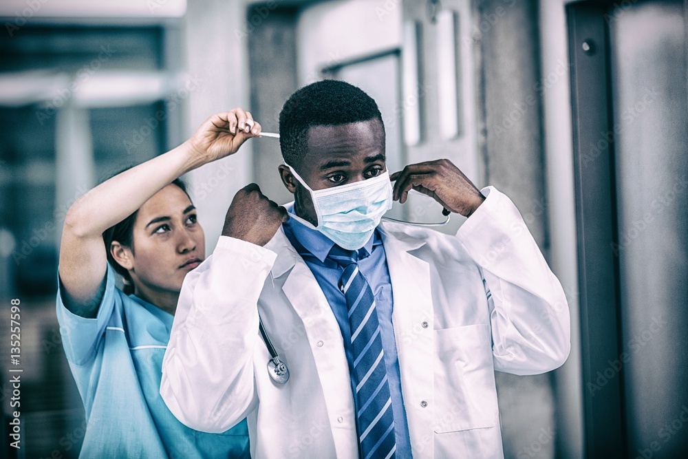 Nurse helping doctor to put on surgical mask