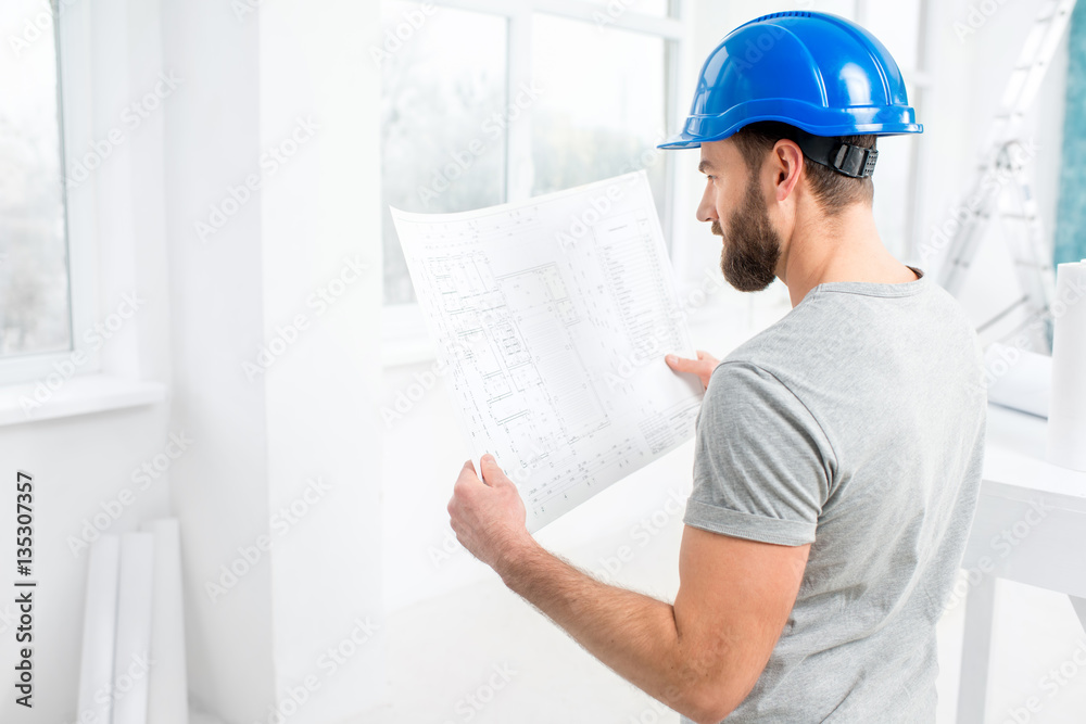 Handsome repairman or builder in helmet working with drawings on renovation of interior