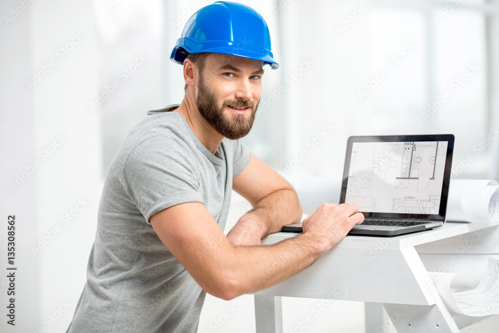 Handsome architect or foreman in helmet working with laptop on the apartment drawings at the structu