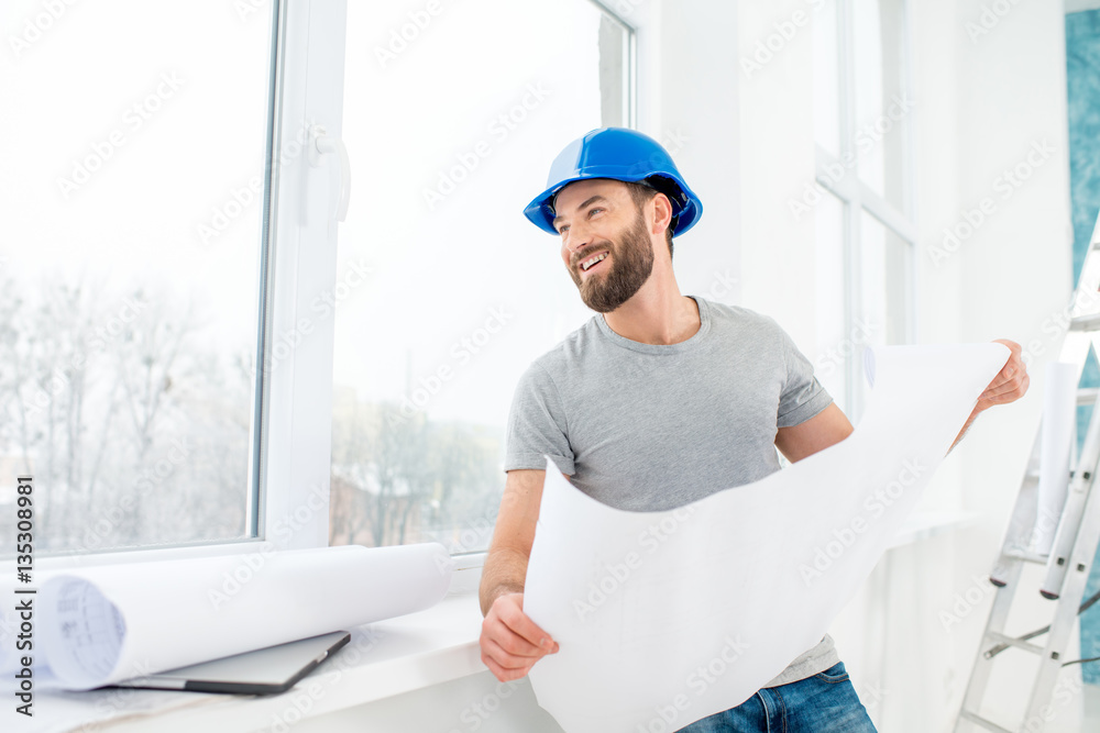 Portrait of a handsome builder, foreman or repairman in the helmet looking at the paper drawings nea