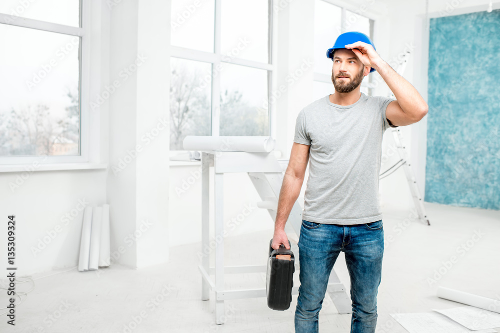 Foreman or worker in uniform with instruments standing in the white interior during the renovation