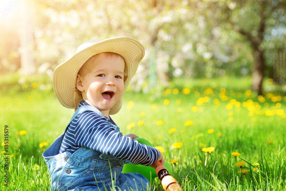 Baby boy sitting on the grass with dandelion flowers in the garden