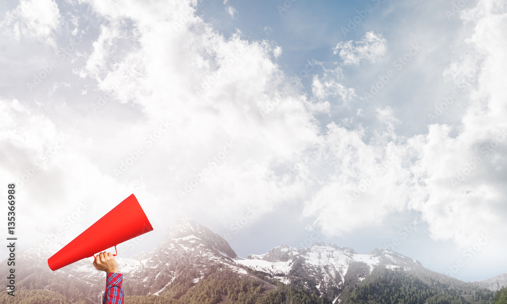 Hand of woman holding paper trumpet against natural landscape background