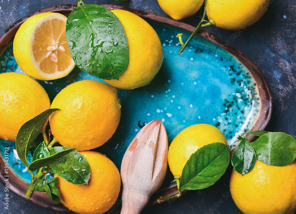 Close-up of freshly picked lemons with leaves in bright blue ceramic plate, top view, copy space, ho