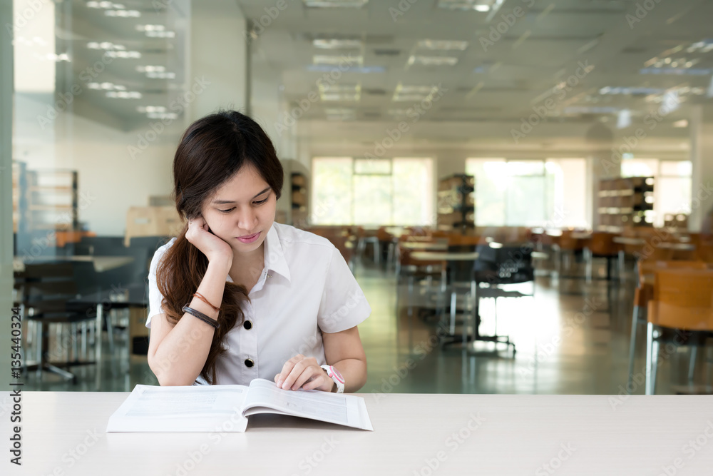 Asian student in uniform reading book in classroom at university