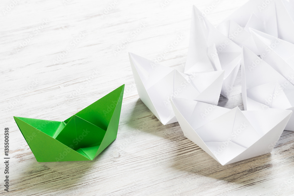 Business leadership concept with white and color paper boats on wooden table