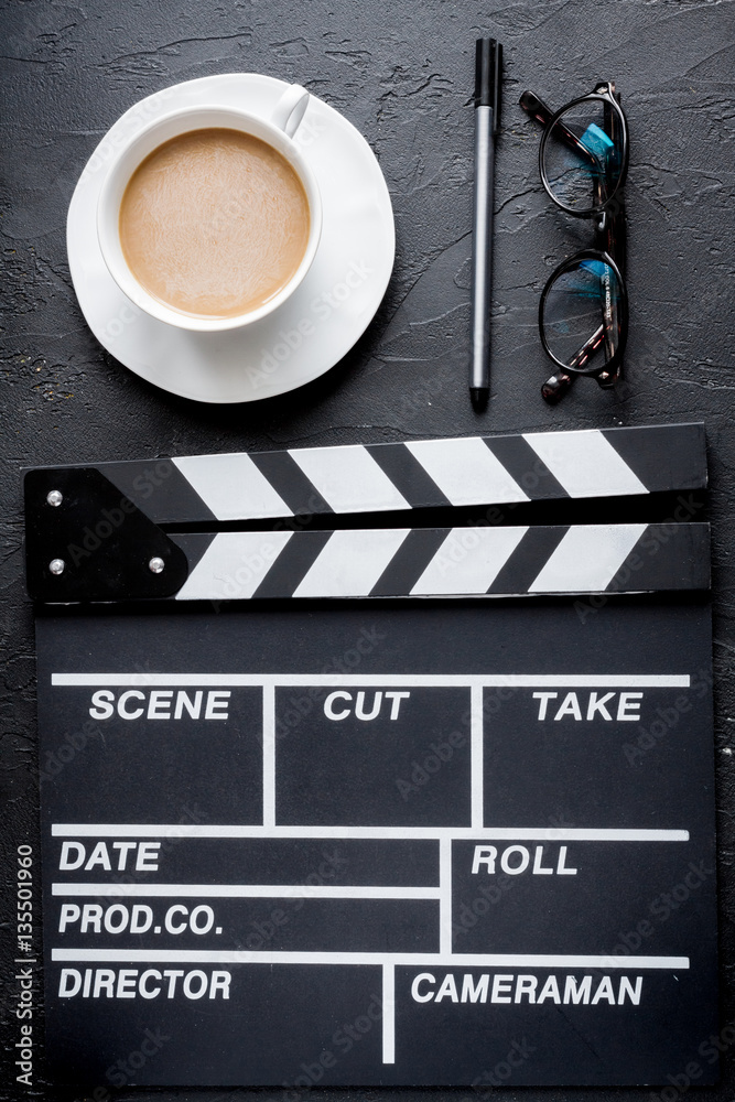 Screenwriter desktop with movie clapper board dark background top view