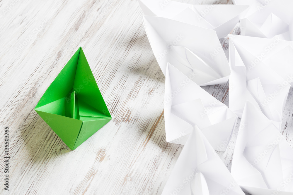 Business leadership concept with white and color paper boats on wooden table